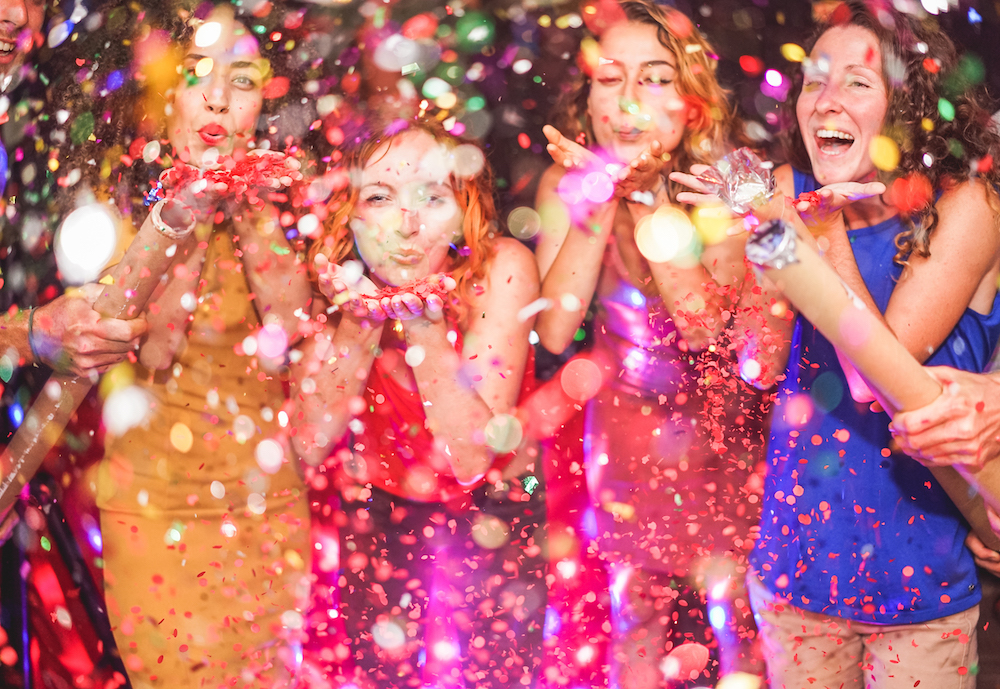 Happy friends making party throwing confetti – Young people celebrating on weekend night – Entertainment, fun, new year’s eve, nightlife and fest concept – Focus on red hair girl hands